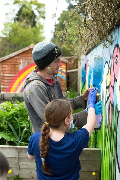 Street artist helping young girl create vibrant artwork in community garden